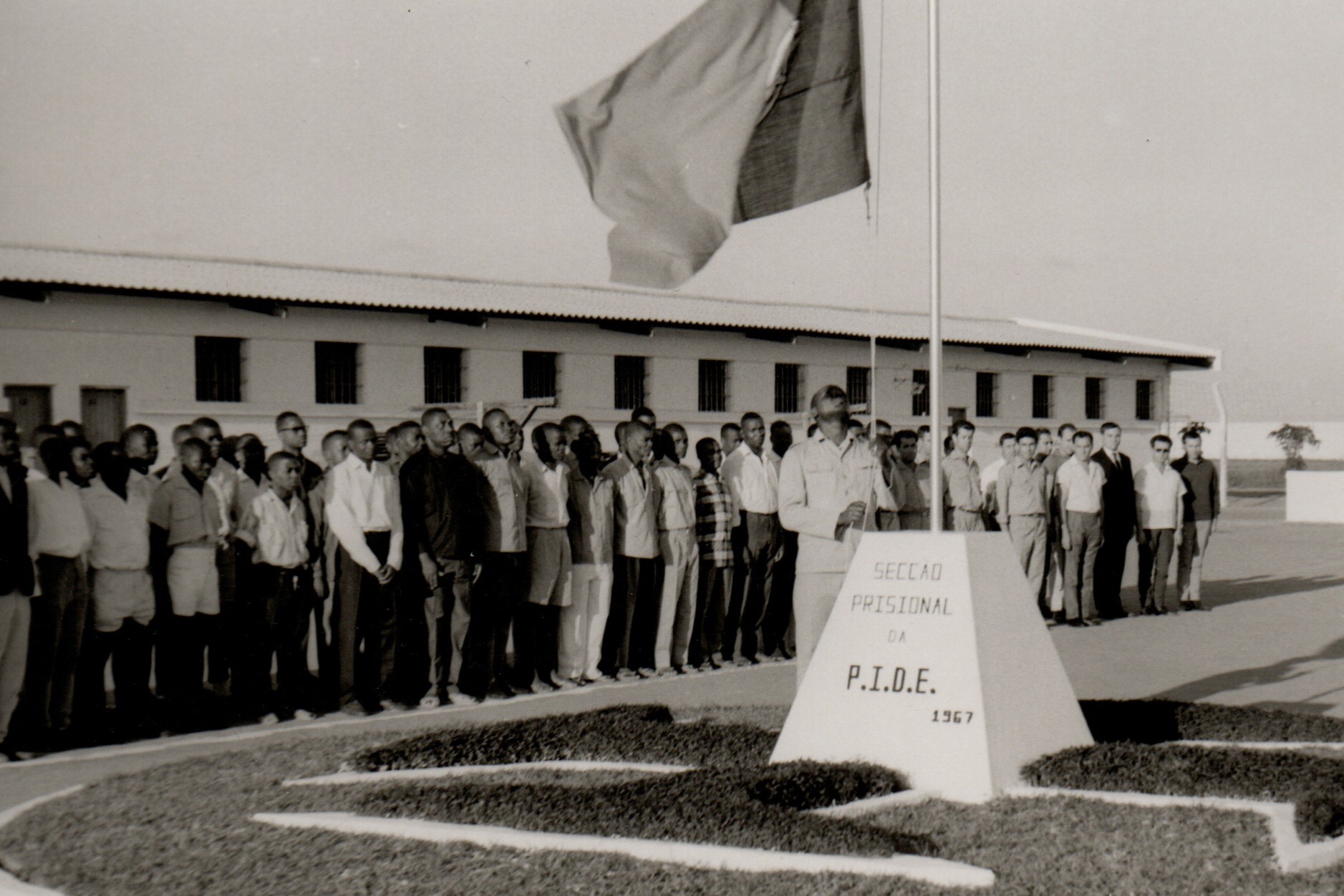 Presos em formatura enquanto um deles iça a bandeira de Portugal durante uma visita oficial à ala prisional da PIDE na Machava